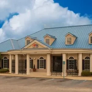 beige building with blue roof with parking lot and trees